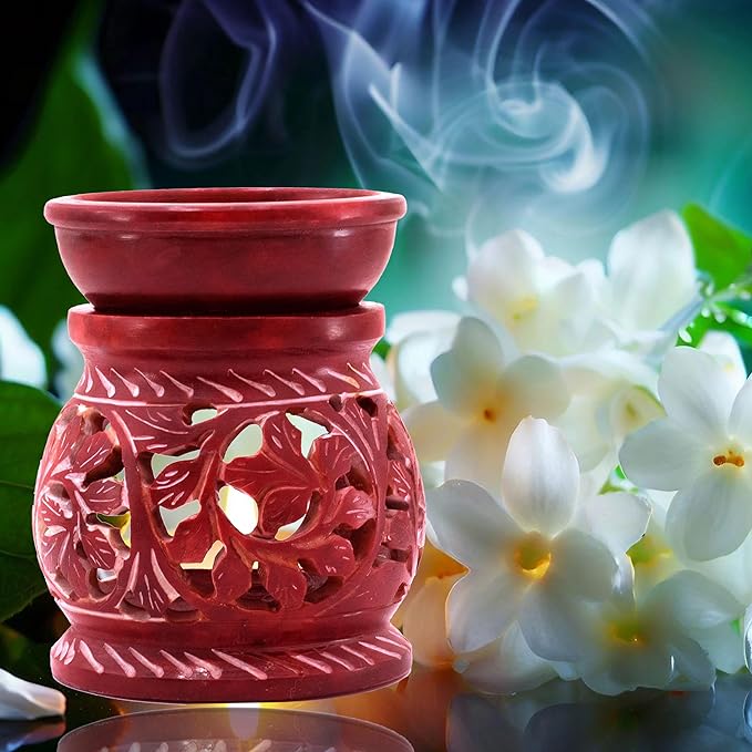 A red, intricately carved tea light oil burner emits white smoke, surrounded by delicate white jasmine flowers. The background features a blend of green and deep blue hues, creating a serene, aromatic indoor fragrance ambiance with the 81bOQ+PAR-L._SX679_.