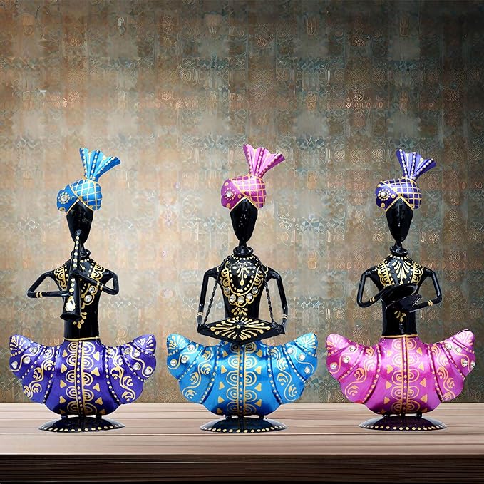 Three vibrantly colored, handcrafted 913tgzH2TJL._SX679_ statues wearing intricate turbans stand on a wooden surface. Each metal figurine has distinct hand positions: one playing a flute, another with hands together in prayer, and the third holding a drum.
